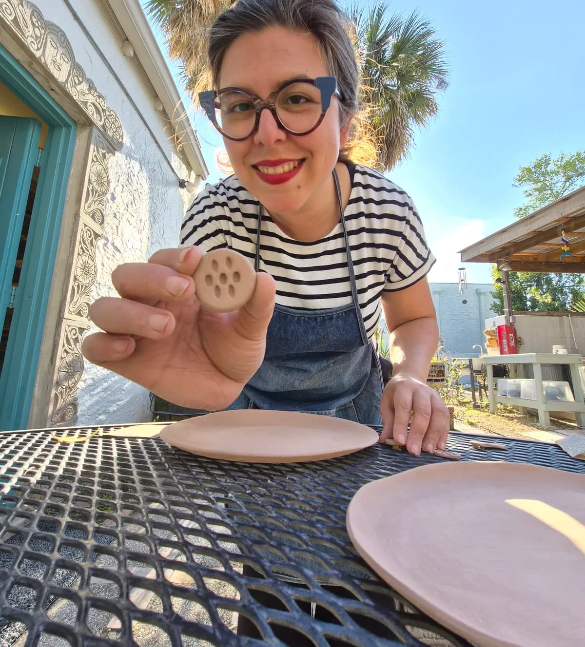 Lynn holding a freshly made ceramic piece outside the studio