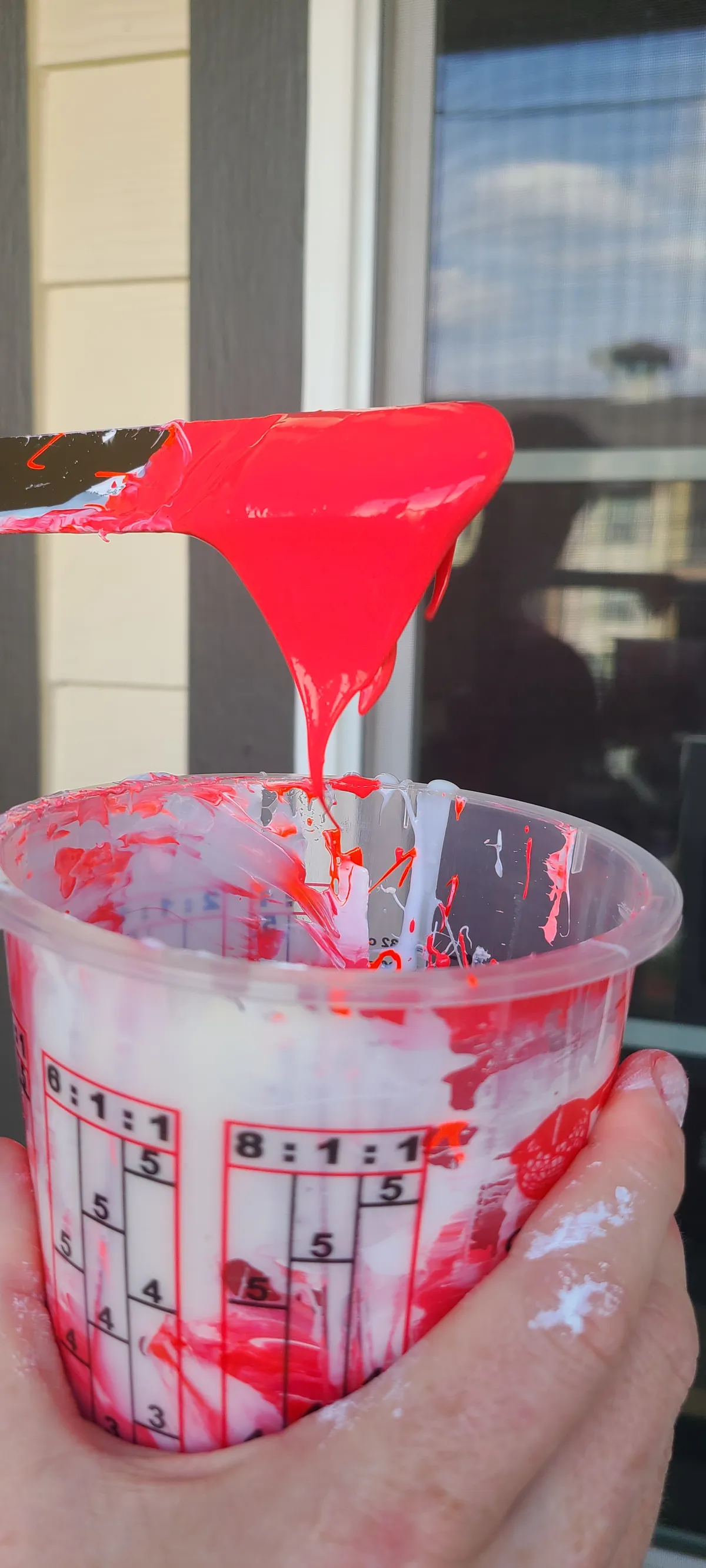Pouring a bright red mix into a measuring cup in the studio